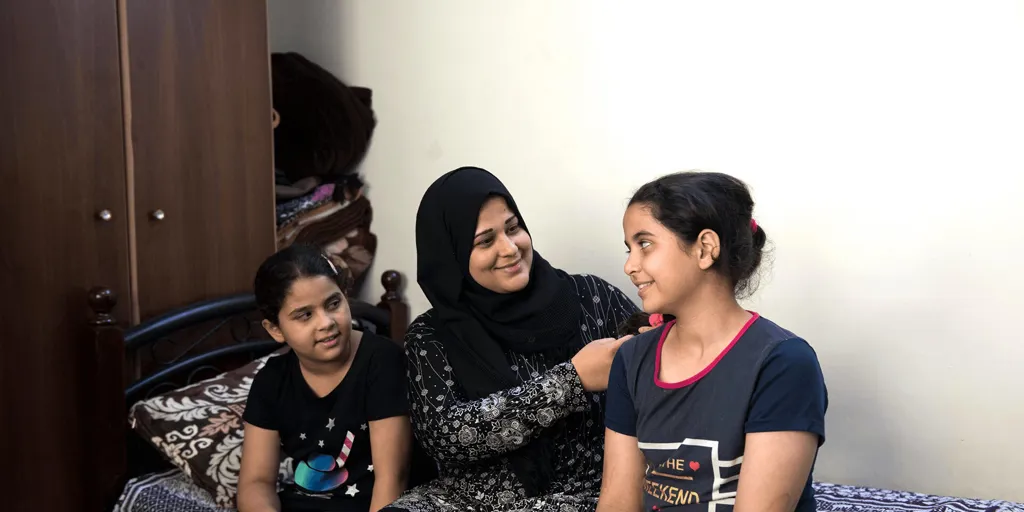 Hanaa and her two daughters sit on a bed