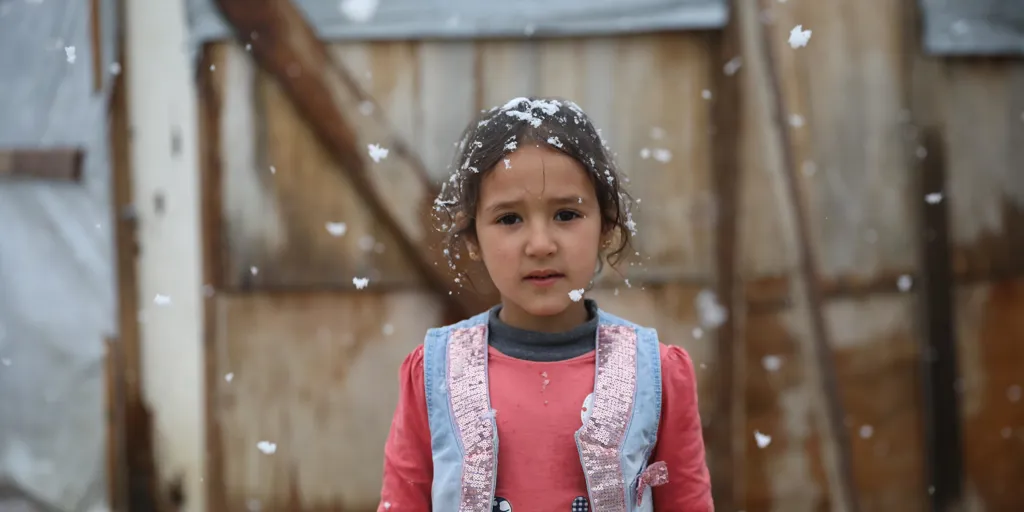 A Young girl stands in front of her tent while it snows in Beqaa valley.